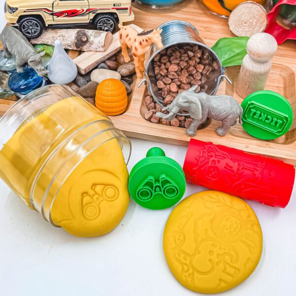 Close-up of yellow handmade Playdough with binocular stamp, safari roller imprint, animal figures, and sensory play accessories from the Animal Adventure Signature Playdough Kit.