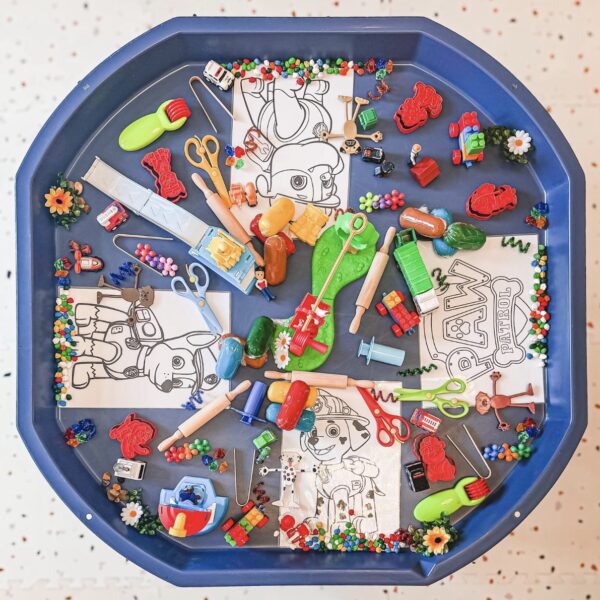 Blue plastic tray overflowing with children's art supplies and small toys around robot-themed coloring pages on a blue tray edge-to-edge.