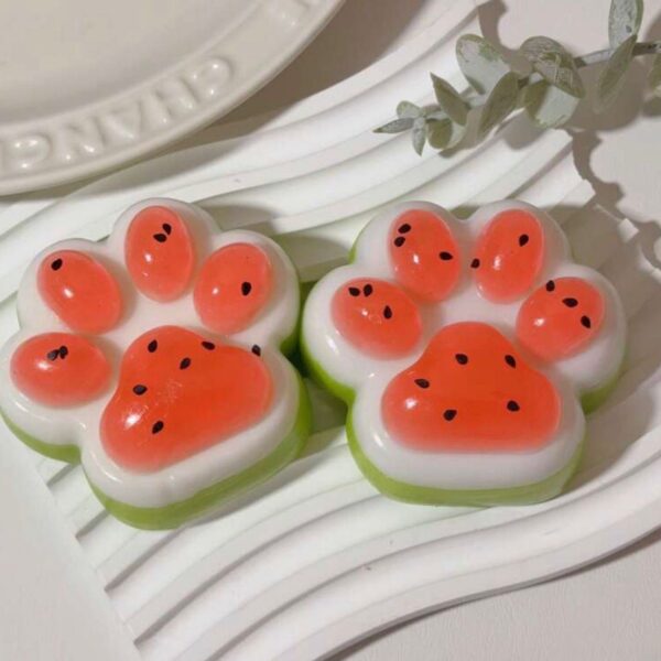 Three paw-print soaps with orange pads on a white base and green edges on a plate.
