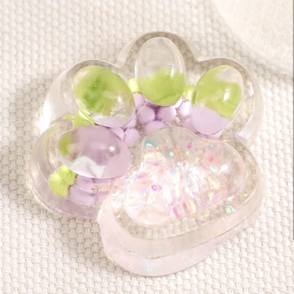 Clear, floral-shaped container holding pastel pink and green marbles with iridescent glitter, on a textured fabric background.