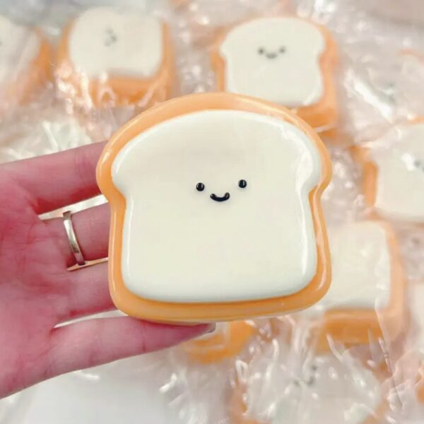 Smiley bread-shaped cookie with orange border and white icing being held in a hand.