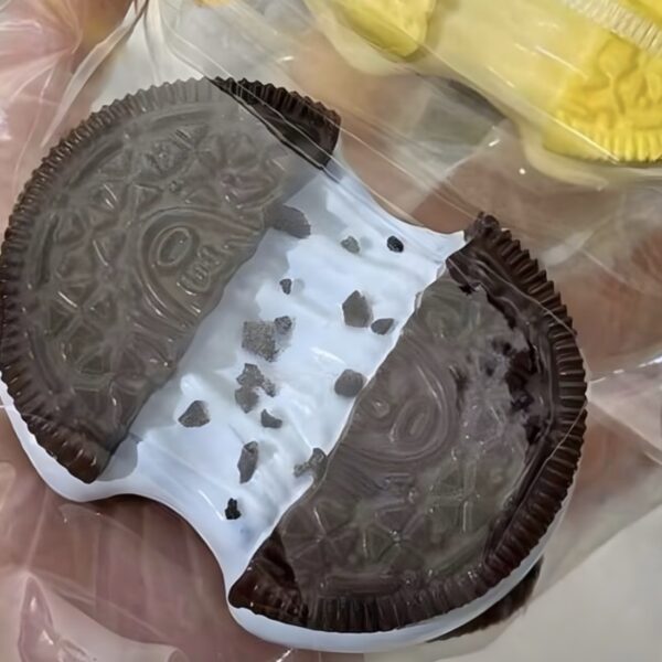 Close-up of a chocolate sandwich cookie with white cream filling and scattered dark crumbs wrapped in plastic.